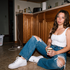Krista sitting on a kitchen floor with a coffee mug, photographed with direct flash in a candid editorial portrait.