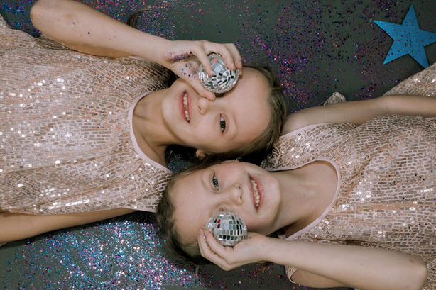 Two girls in sequined dresses holding disco balls, smiling at the camera.