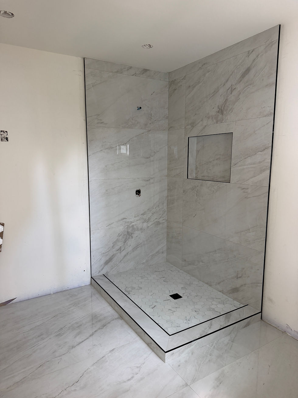 Completed marble-look tiled shower with niche and raised shower base