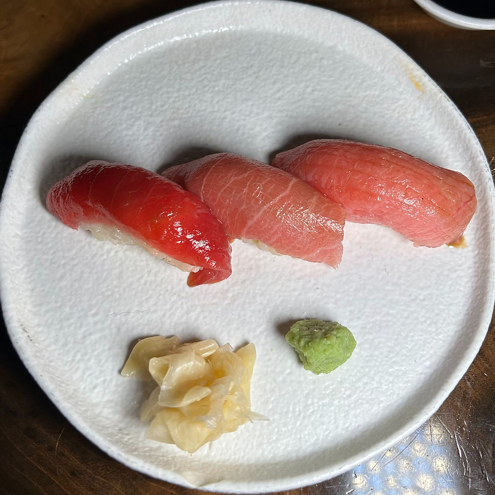 Three pieces of tuna sushi on a plate with ginger and wasabi.