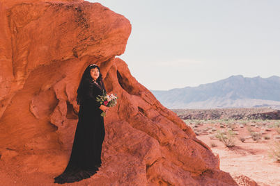 Woman in black dress poses near red rock formations Valley of Fire Ceremony.