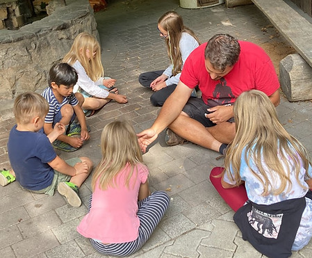 Kinder sitzen mit dem Archäologen Konstantin und spielen mit selbst gemachten Würfeln.