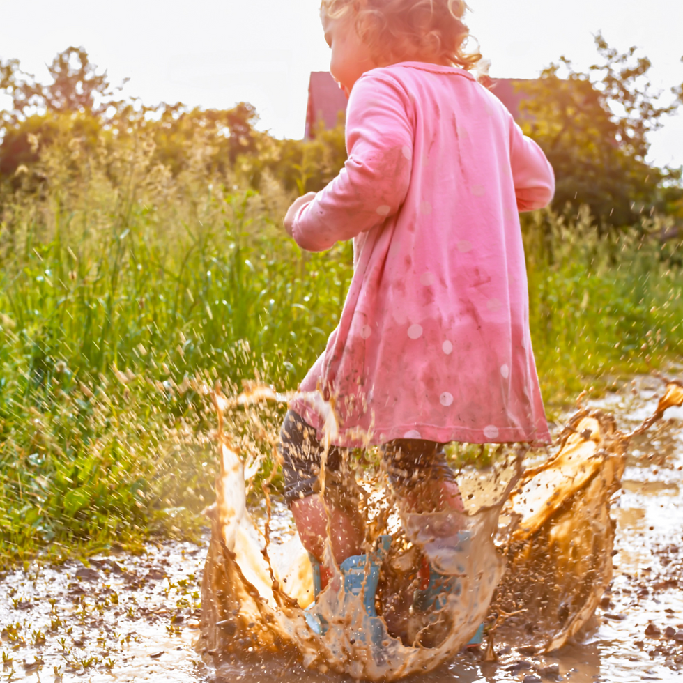little girl jumping in a muddy puddle
