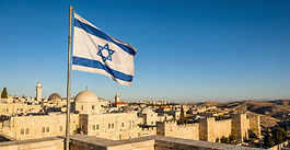 A crisp winter morning view over Jerusalem, featuring an Israeli flag waving proudly in the foreground against a deep blue sky and the ancient stone city.