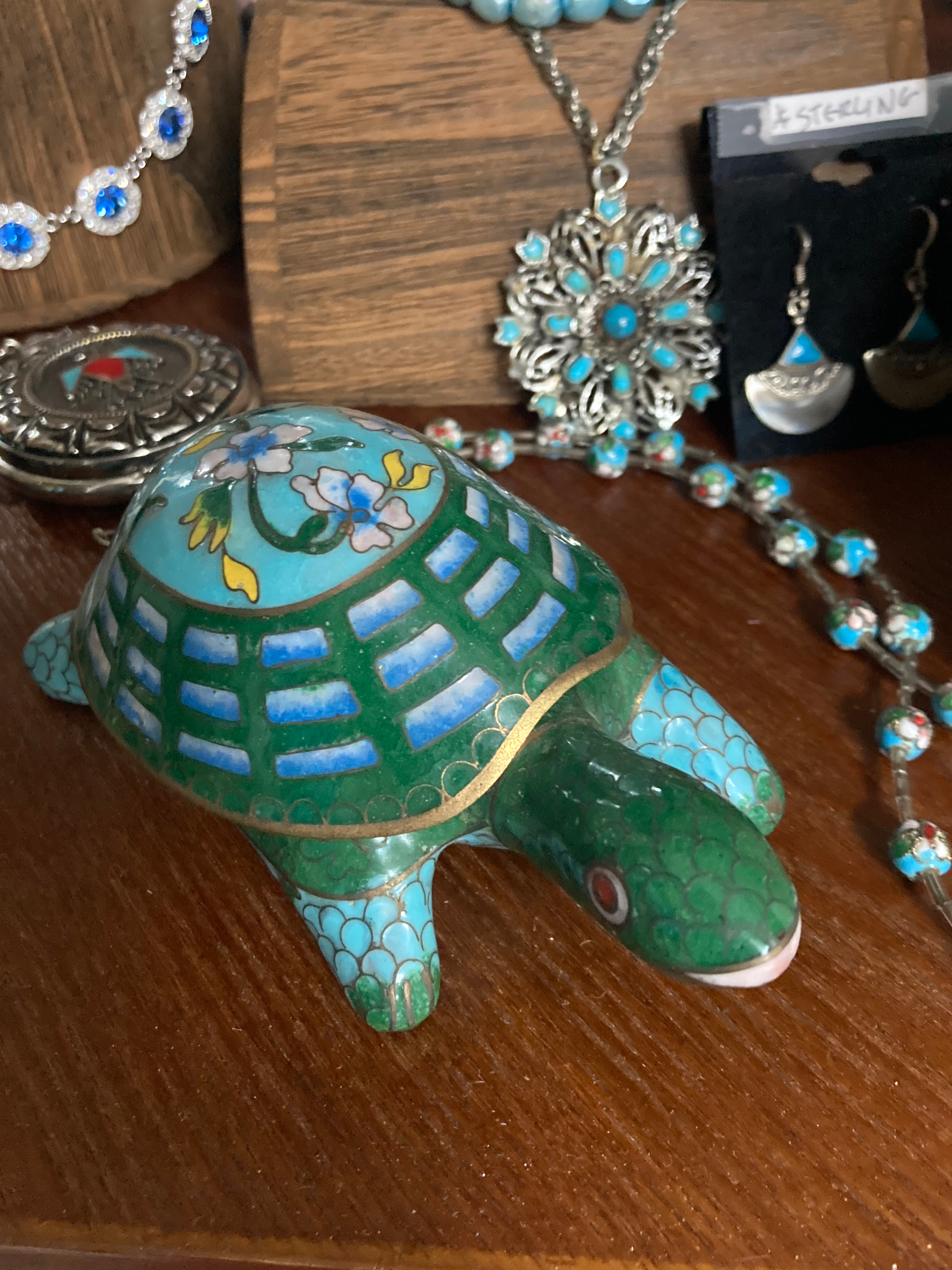 Vintage cloisonné turtle trinket box with vibrant green and blue enamel, floral design on shell, and detailed metalwork, displayed among turquoise jewelry.
