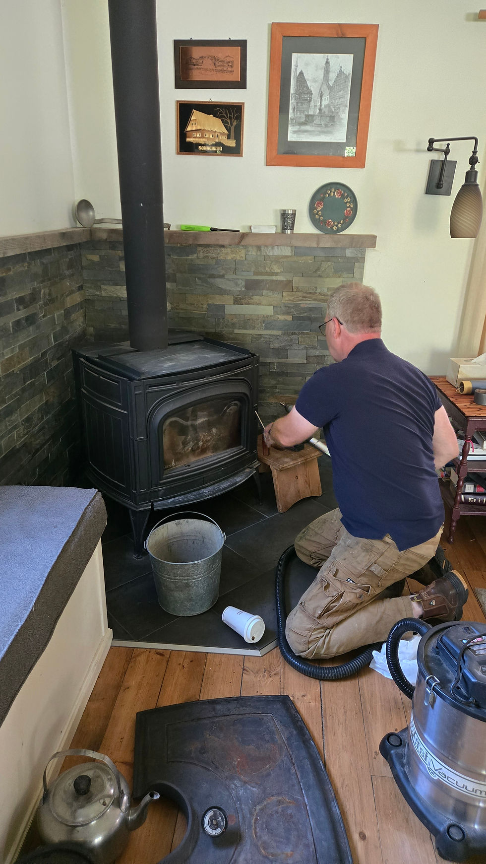 Kneeling to clean and service a wood stove during a maintenance visit