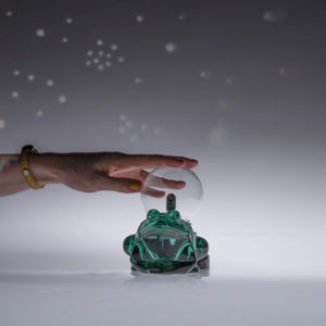 Green glass frog with a small plasma ball inside, and an arm reaching to tough the plasma ball