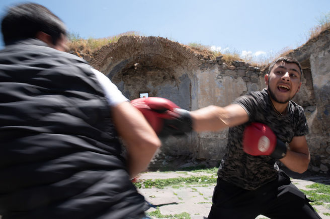 Two boys train boxing inside an improvised arena: a crumbling old church beside a cemetery.

Armenia, 2024.