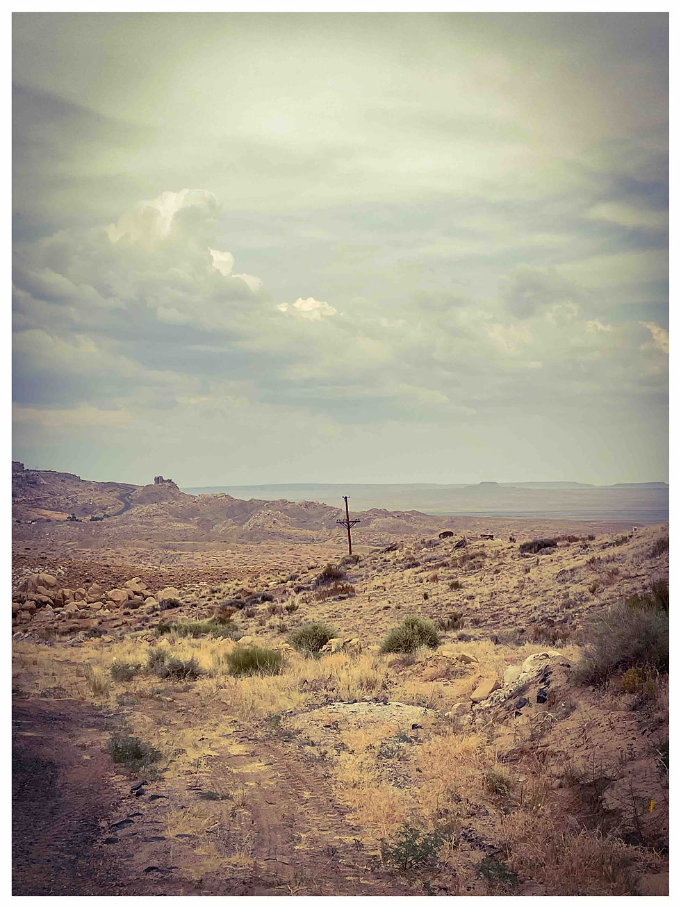Sur cette terre ocre, un seul poteau se dresse, sentinelle solitaire. Il est là pour recevoir le message du ciel et nous le murmurer, à nous qui marchons sur la terre. Les nuages, immenses et chargés, nous rappellent que le sacré est partout, même sur un chemin battu.