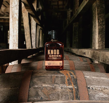 Image of a bottle of Knob Creek Whiskey sitting on a row of barrels