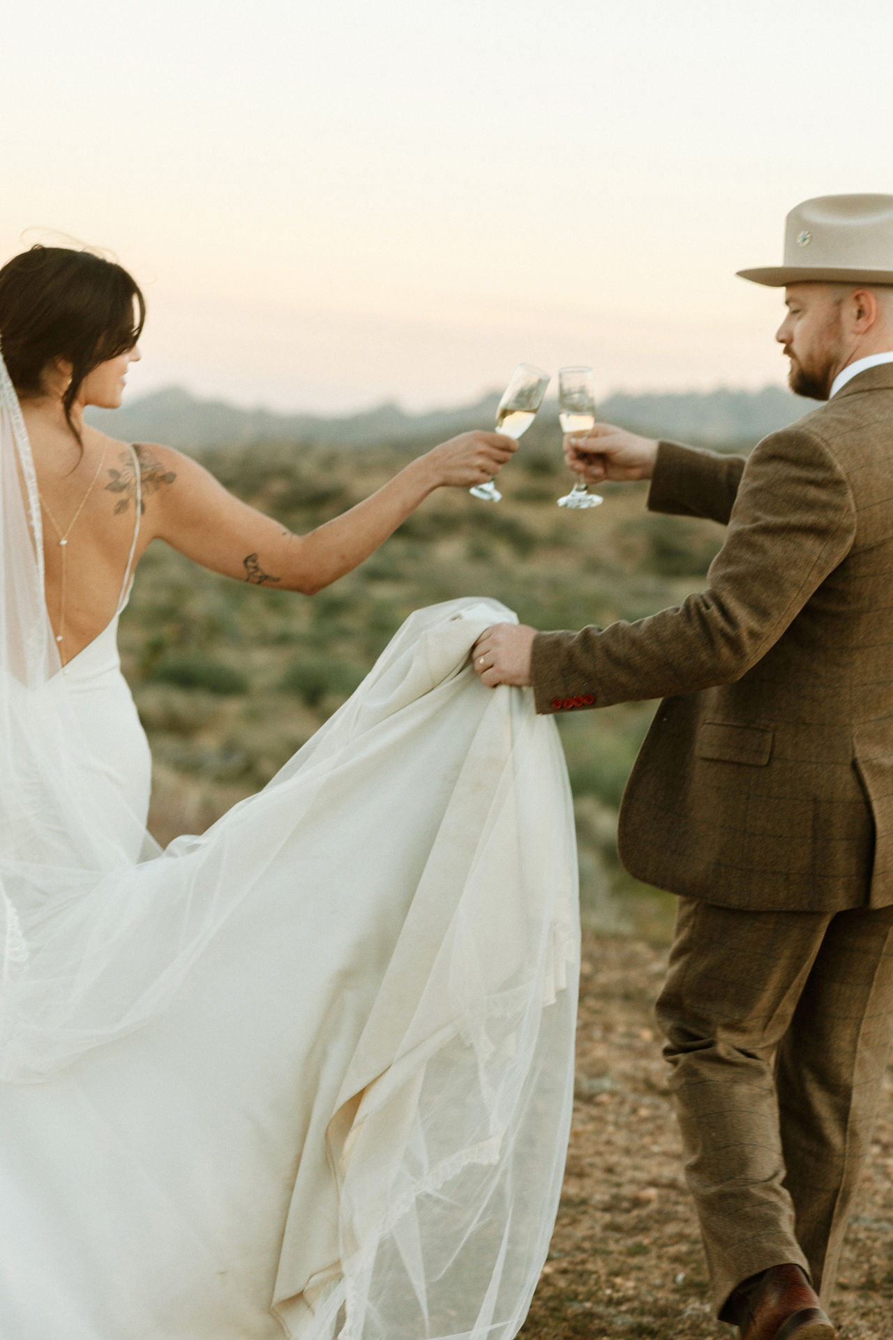 bride and groom clinking champagne glasses as they walk through the joshua tree desert