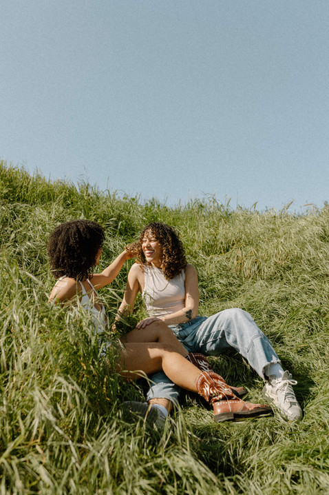 lesbian couple sitting in field looking at one another