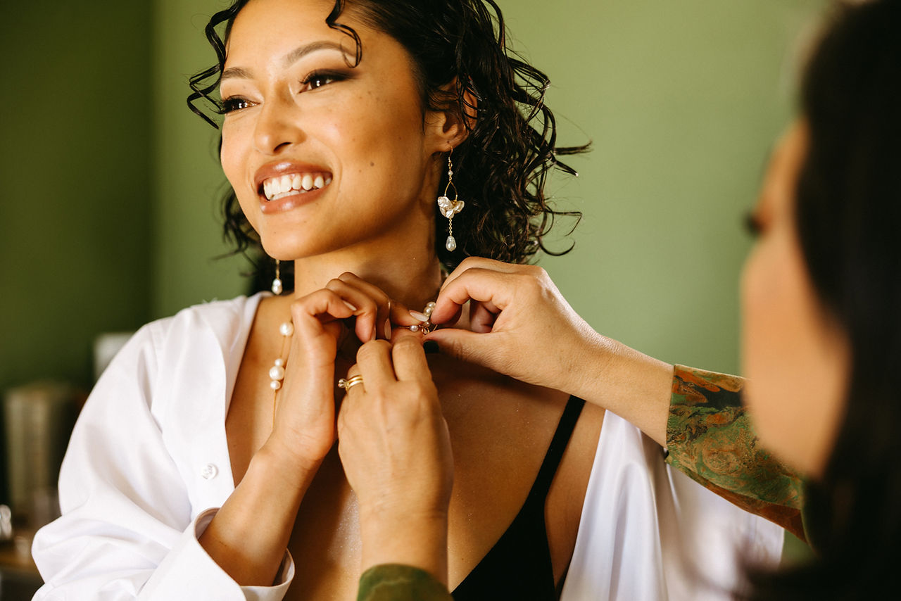 mom helping bride with short curly hair put on her necklace