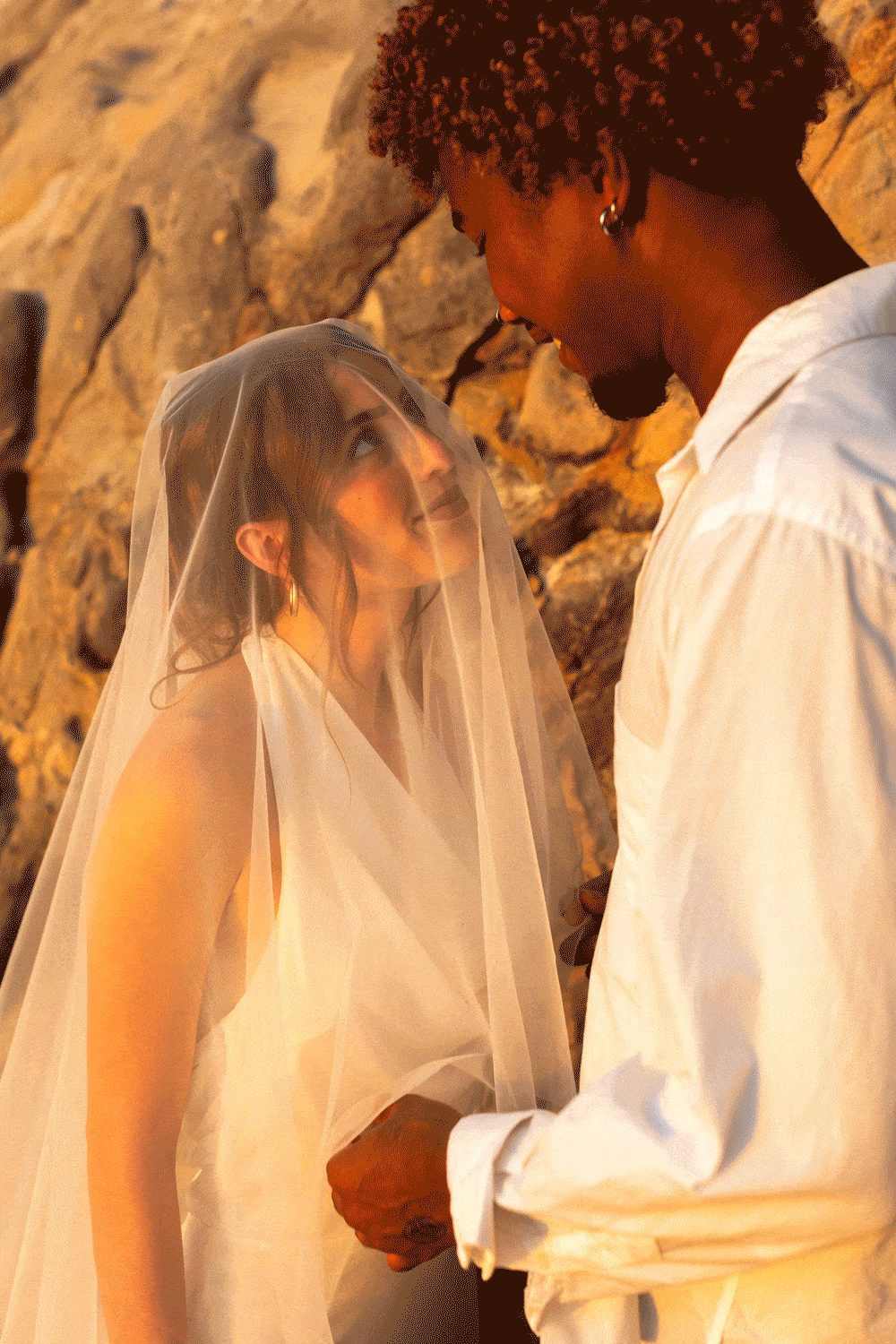 groom lifting bride's veil and kissing her on the beach