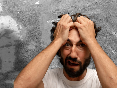A man gripping his head with both hands, displaying a distressed expression. Gray textured background, wearing a white shirt.