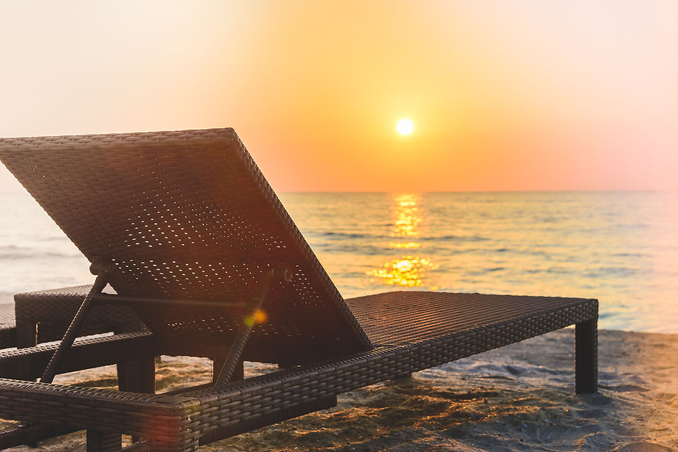 Wicker lounge chair on a calm beach at sunset, with golden sun reflecting on the sea and a peaceful orange sky.