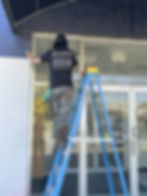 Clean Vault Solutions team member cleaning exterior windows of a commercial building using a ladder.