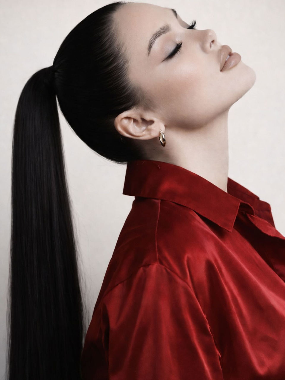 Mujer elegante con cola de caballo alta y camisa roja satinada.