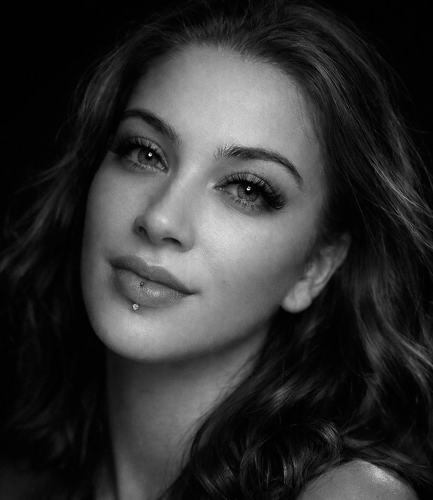 Retrato en blanco y negro de mujer con piercing, cabello ondulado.