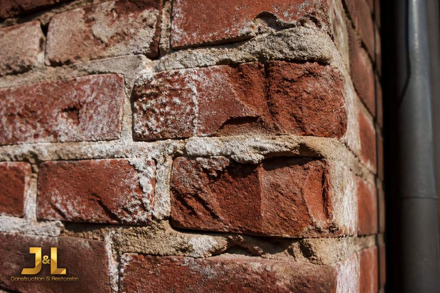 Close-up of deteriorated historic brick wall showing spalling brick faces, white efflorescence staining on mortar joints, and crumbling mortar separating from weathered red brick in sunlight