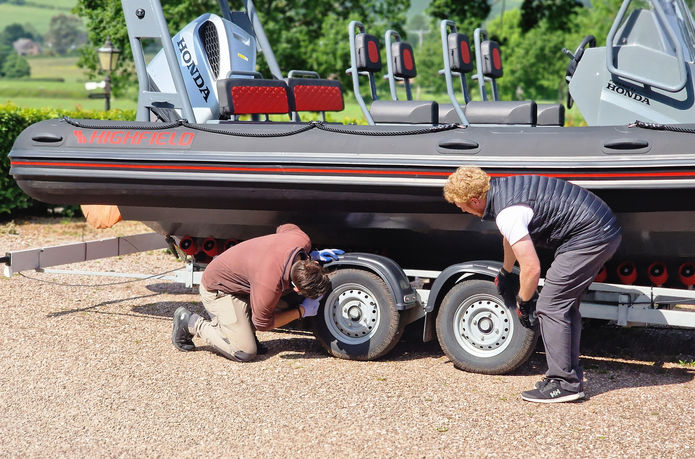 Two guys inspecting trailer tyres on a boat trailer.