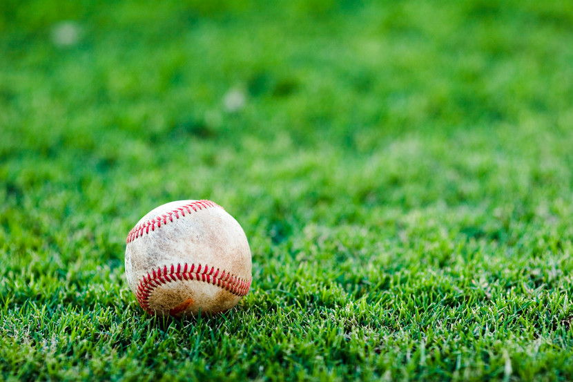 A worn baseball rests on a lush green grass field.