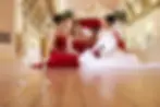 Example of Event Photography. wo glasses of champagne sit on a polished wooden floor in the foreground, with four women in red gowns blurred in the background.