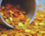 A warm, golden-hued photograph of gold coins spilling from a pot