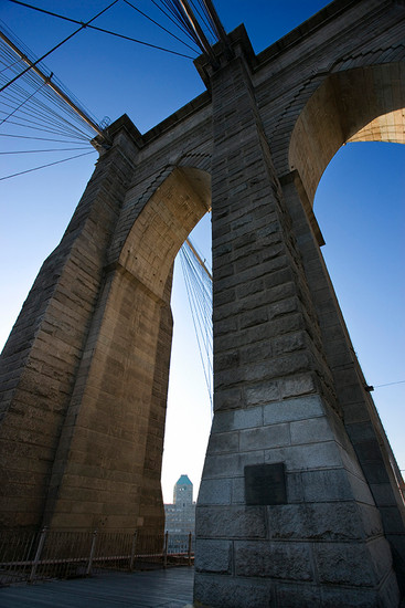 Stone arch of the Brooklyn Bridge against the sky.