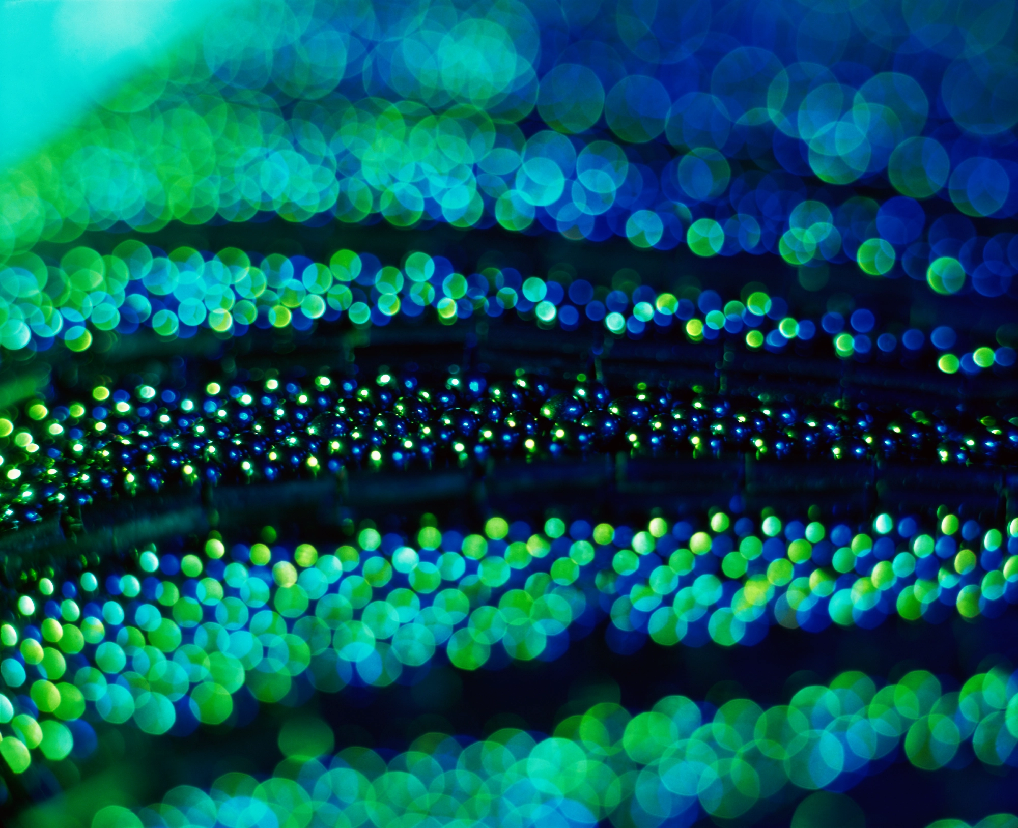 An abstract close-up of blue and green bokeh lights creates a shimmering, textured pattern. 