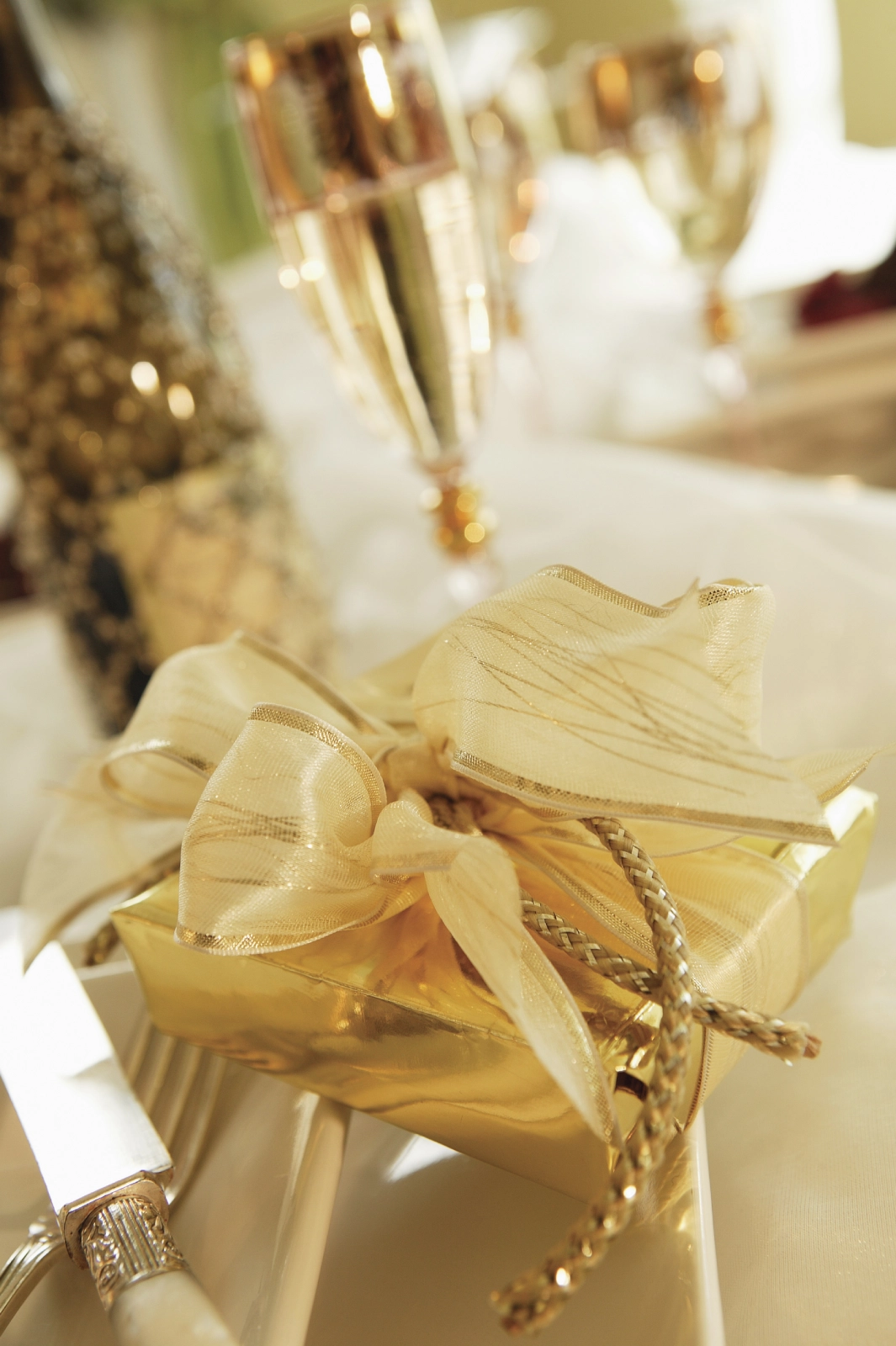 A beautifully wrapped golden gift with a ribbon sits on a table alongside elegant champagne flutes and a bottle