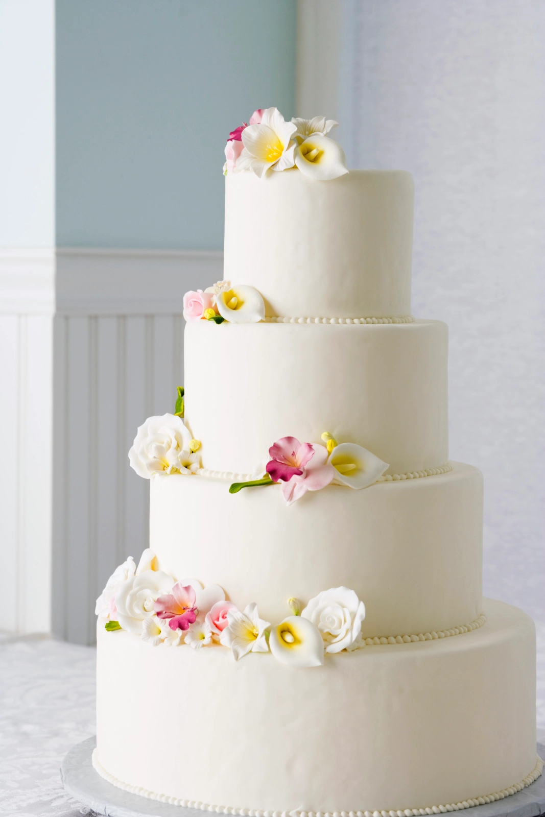 A four-tiered white wedding cake adorned with delicate flowers in pink and white.
