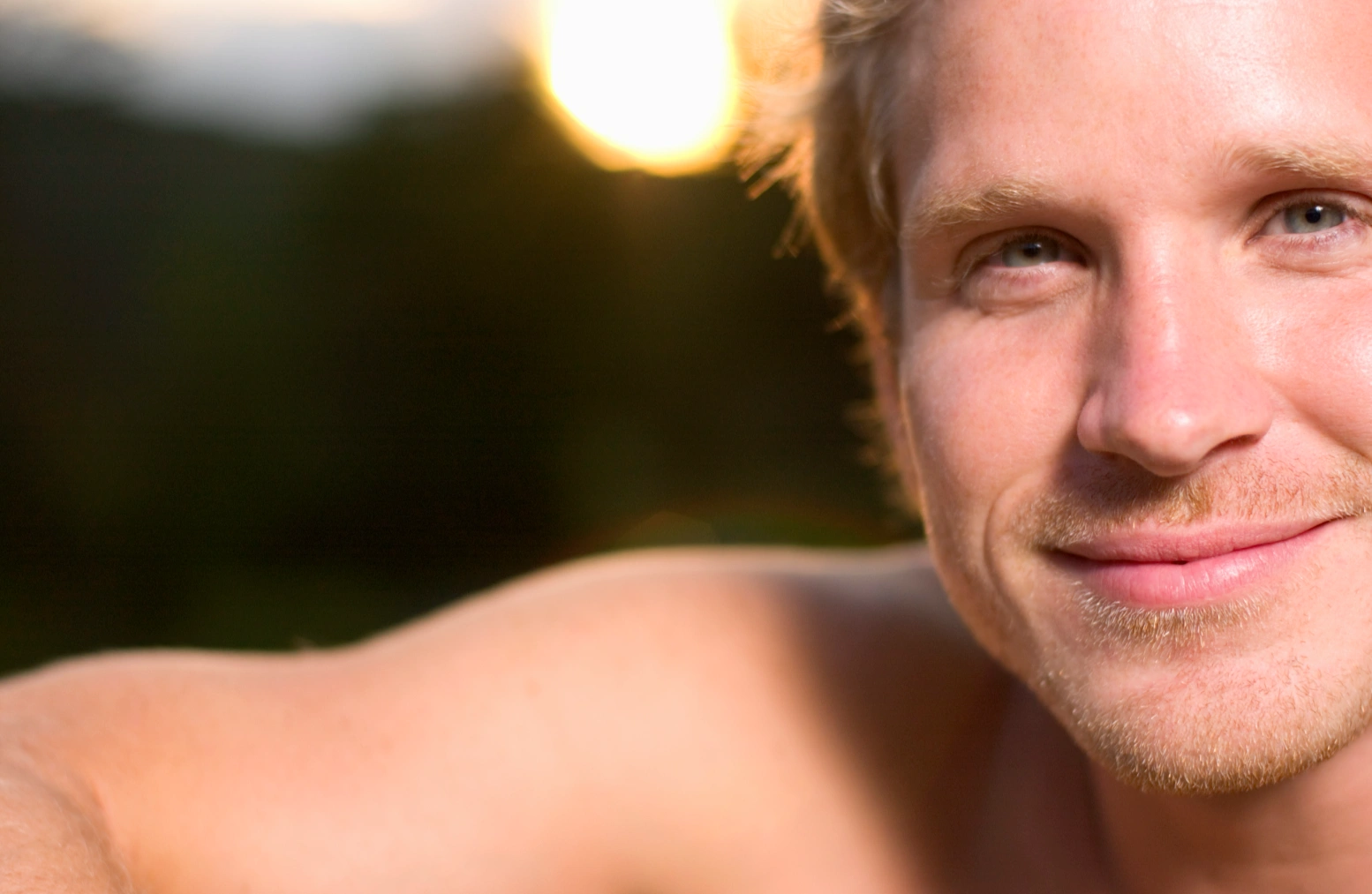 A close-up of a smiling young man with a light tan and short, messy blond hair. 
