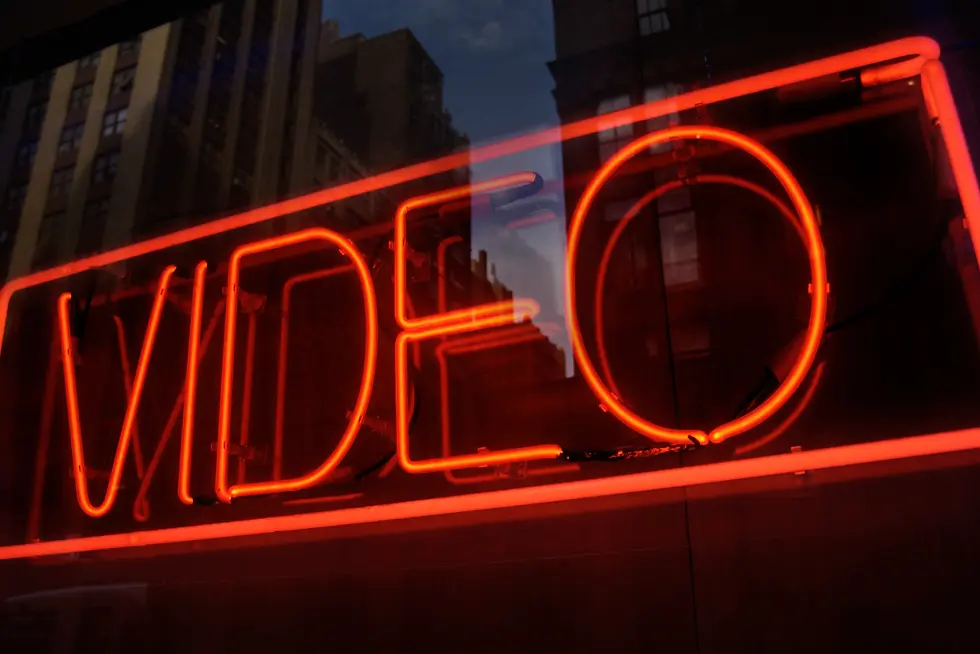 A glowing red neon "VIDEO" sign illuminates a cityscape reflection in a window,
