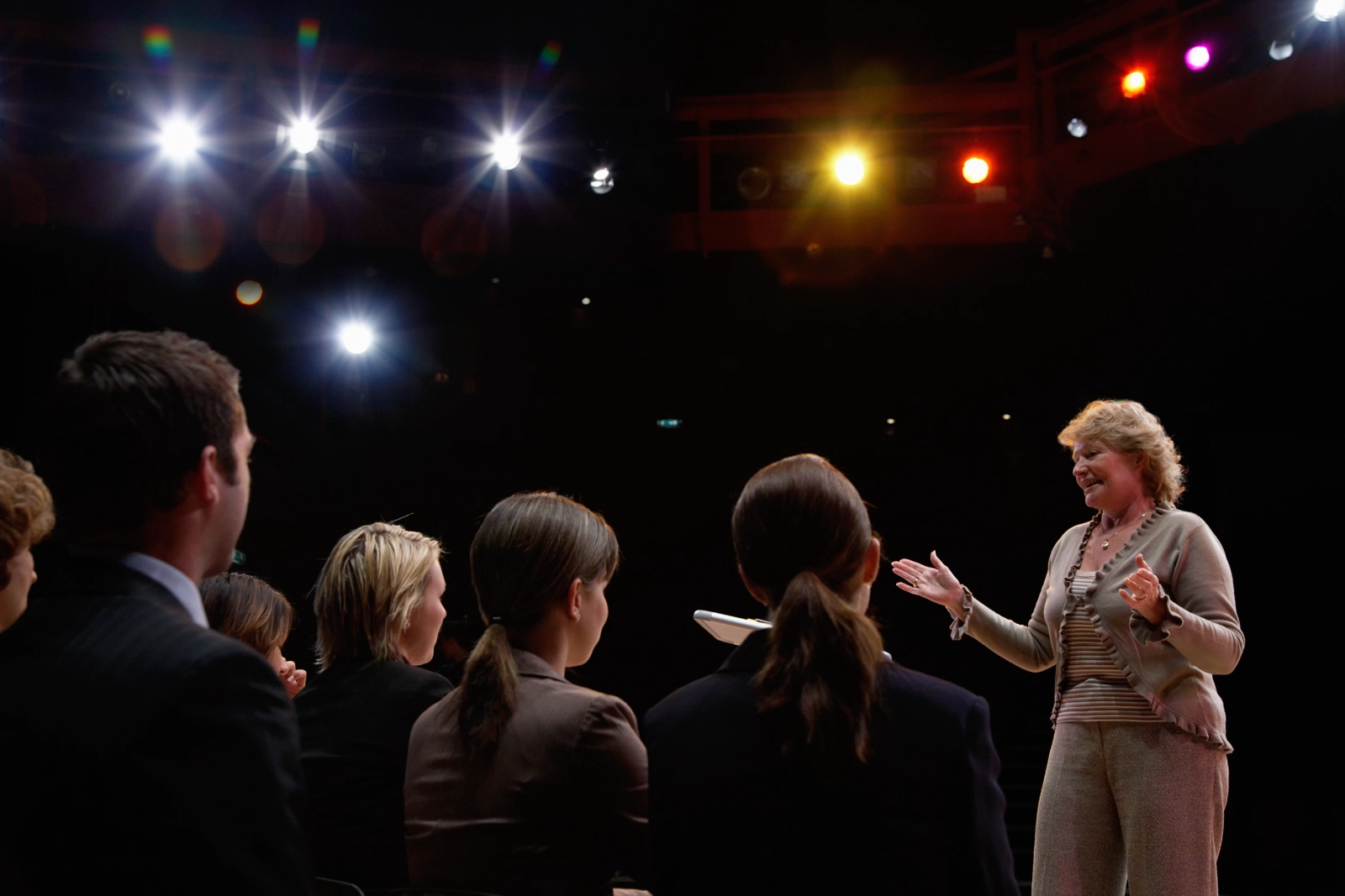 A woman stands on stage, gesturing while speaking to an audience.