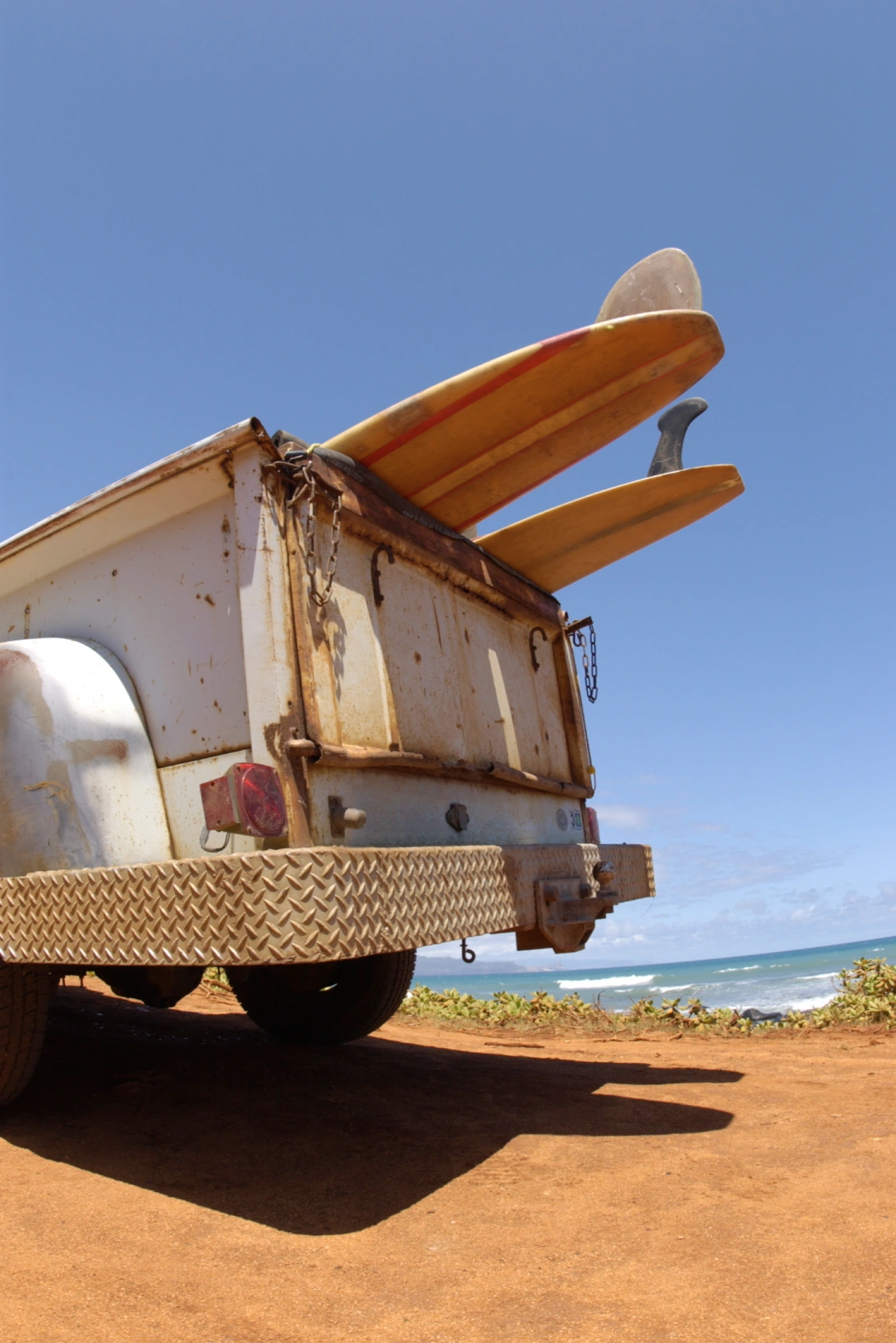 A weathered trailer with rusty surfaces holds two vibrant surfboards against a clear blue sky, overlooking the ocean. 