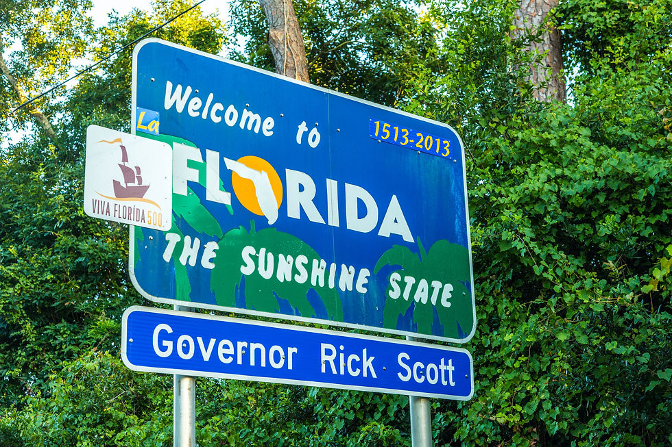 Blue Florida welcome sign reads "The Sunshine State," forest background, small Viva Florida 500 sign, "Governor Rick Scott" noted.