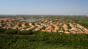 Aerial view of a suburban neighborhood with orange-roofed houses, surrounded by lush Everglades mangroves and a small lake under a clear blue sky.