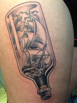 Neo-traditional black and grey clipper ship sailing in water framed inside a corked bottle on the top thigh.