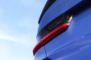 Closeup of a back left tail light of a blue car against a blue sky