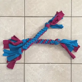 Blue and magenta braided rope dog toy on a beige tiled floor, with frayed ends and a playful look.