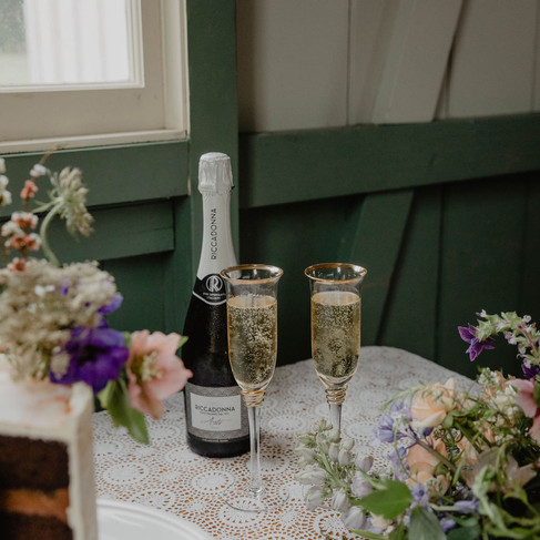 Two glasses of freshly poured bubbles stand beside the small wedding cake.