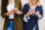 female-friends-leaning-wall-using-smartphone.jpg