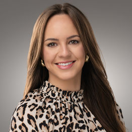 Professional business headshot of woman in patterned blouse, studio background