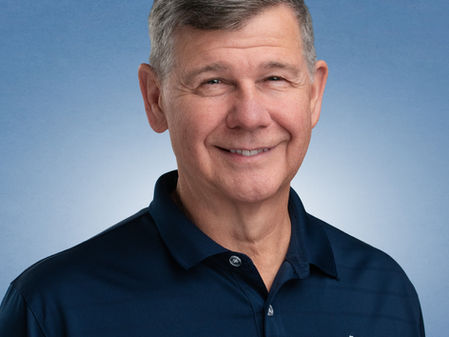 Professional older male headshot in navy polo on blue background