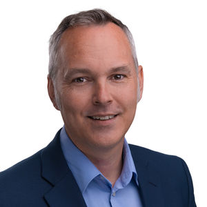 Professional business headshot of a man in a blue blazer, smiling against a light background