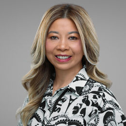 Professional business headshot of woman with long highlighted hair, studio background
