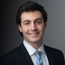 Professional business headshot of a man in a suit and tie, smiling against a dark background