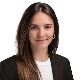 Professional headshot of a woman with long brown hair wearing a black blazer, subtle smile against a light background