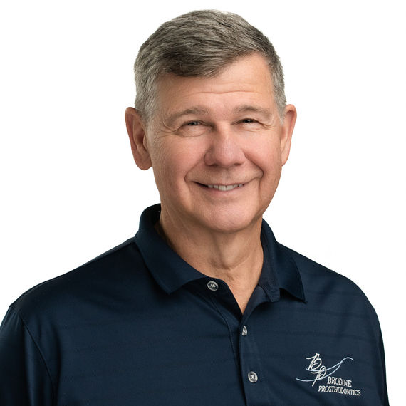 Professional headshot of a man with short gray hair wearing a dark polo shirt, smiling against a light background